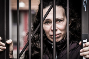 Daniela Mitterlehner - Frau blickt traurig durch Gitterstäbe